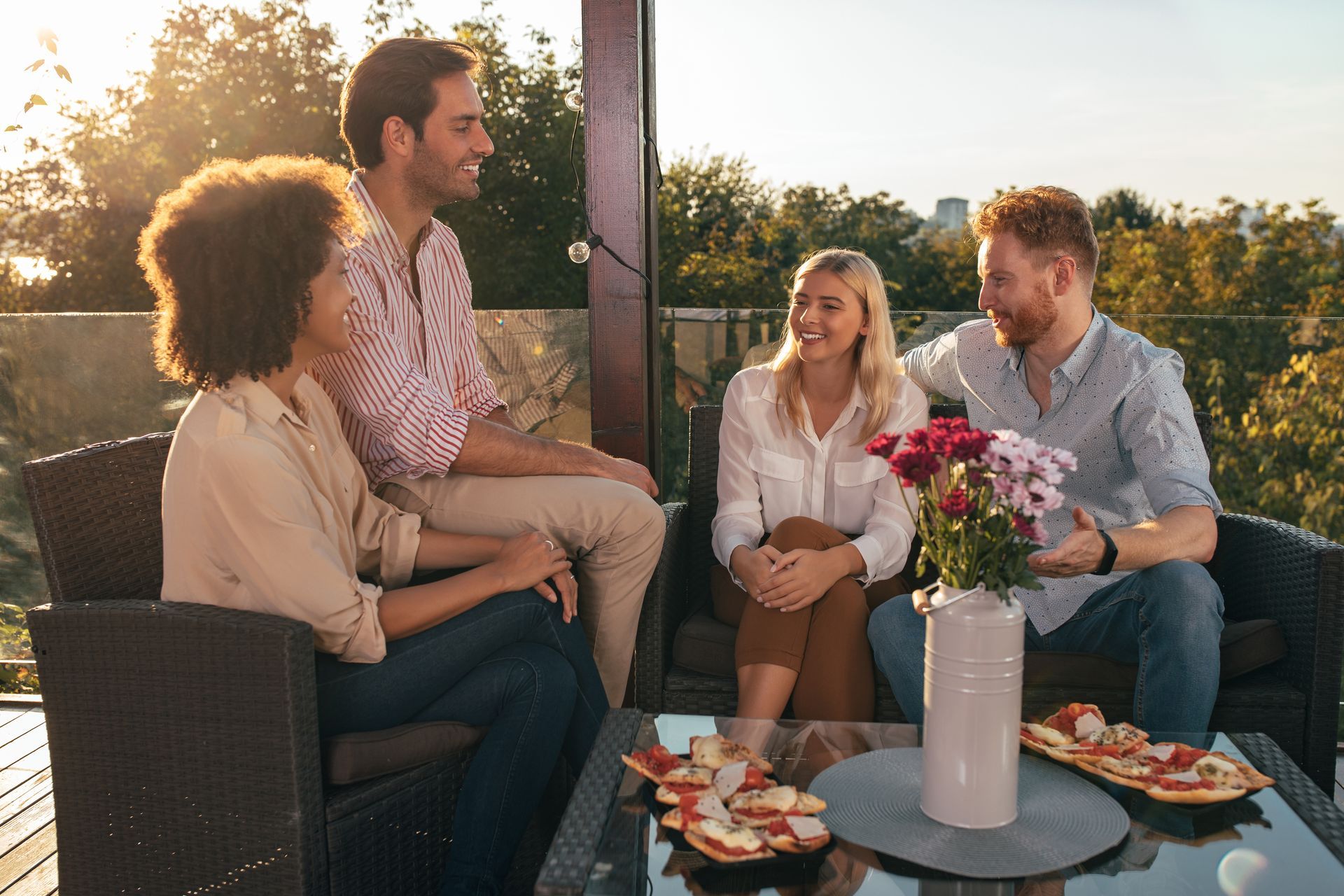Friends chatting on a patio at sunset with drinks and appetizers on a glass table
