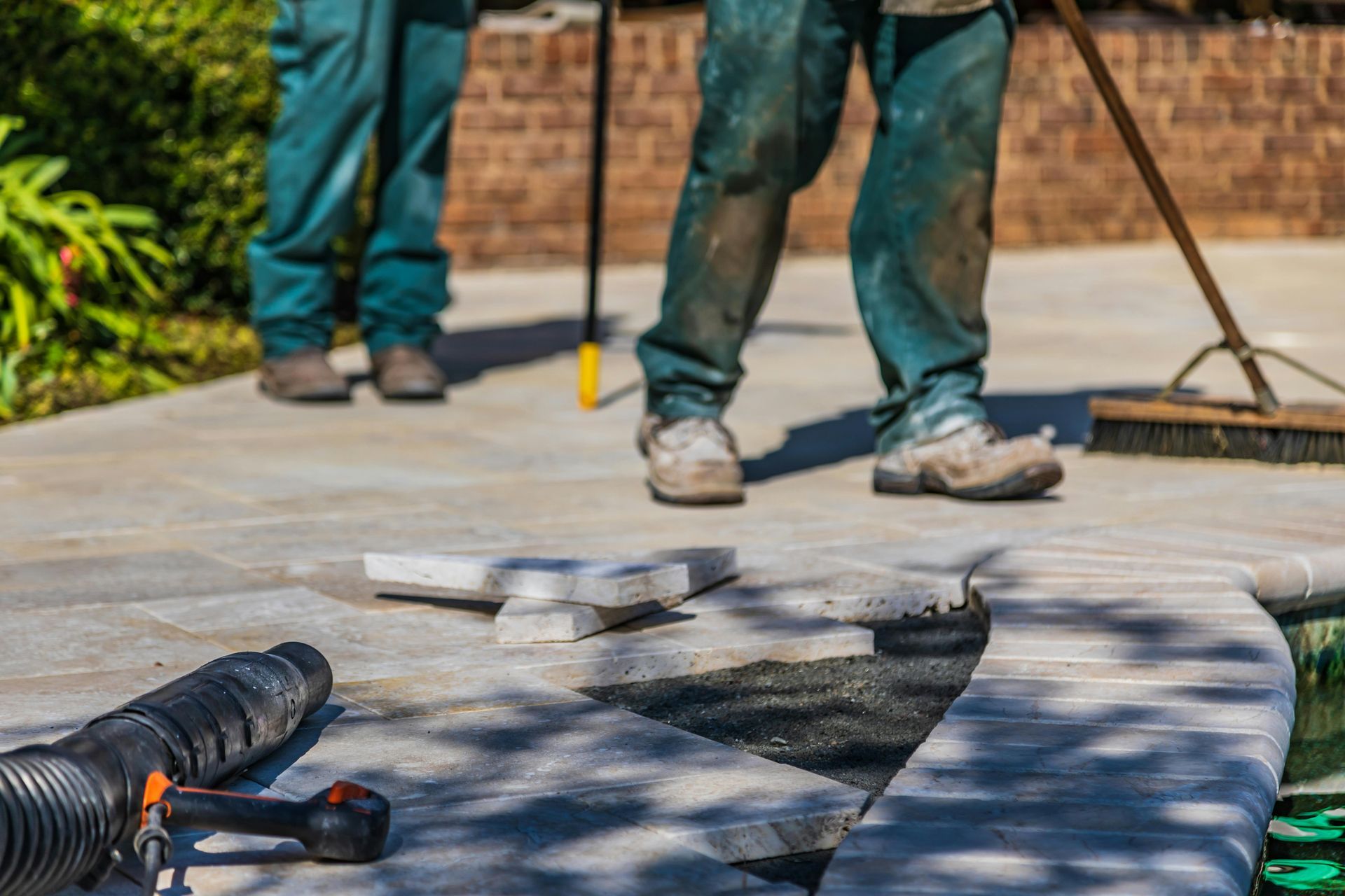Workers installing a curved stone patio border with tools on a concrete surface