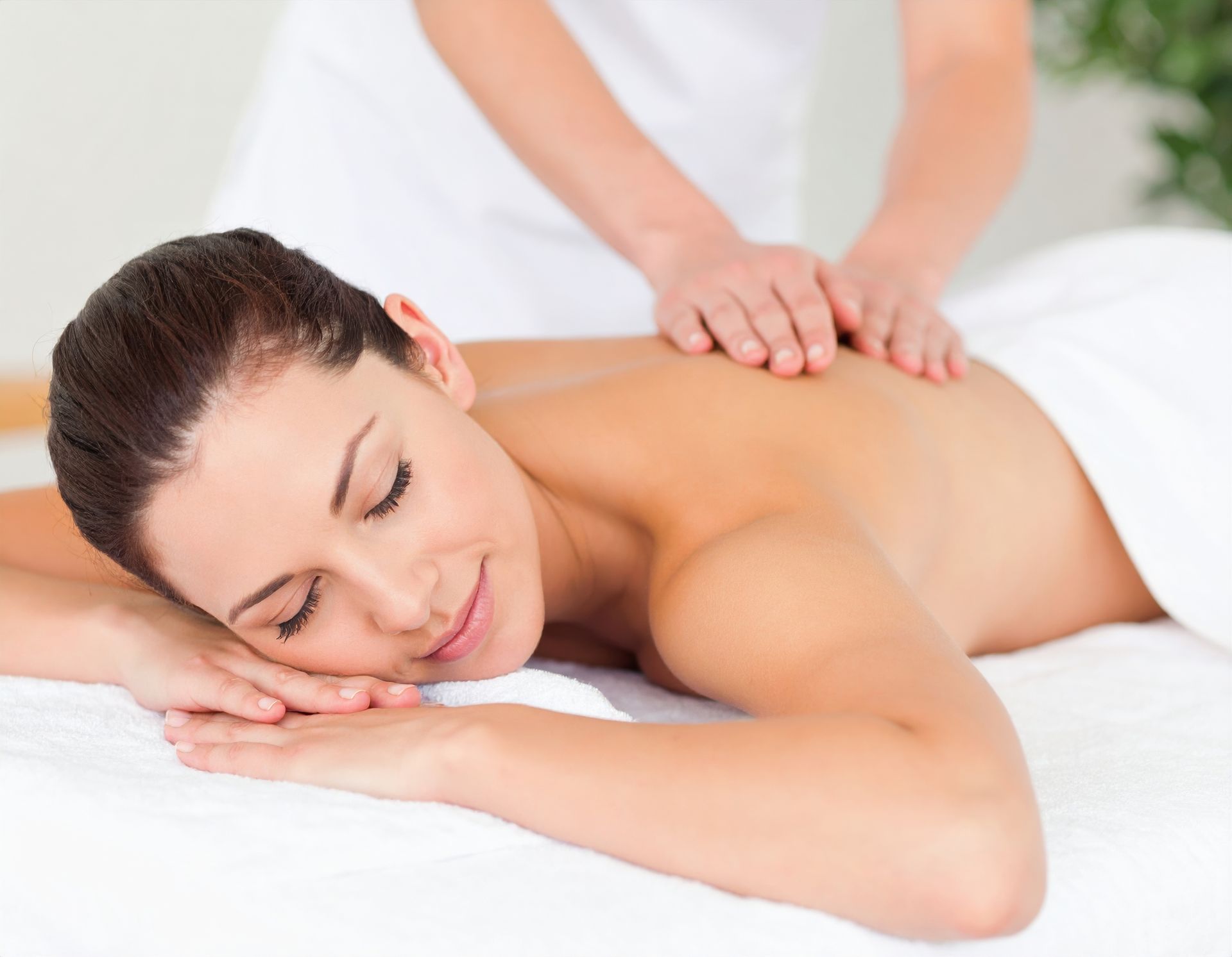 Woman receiving a back massage in a spa setting; closed eyes, smiling.