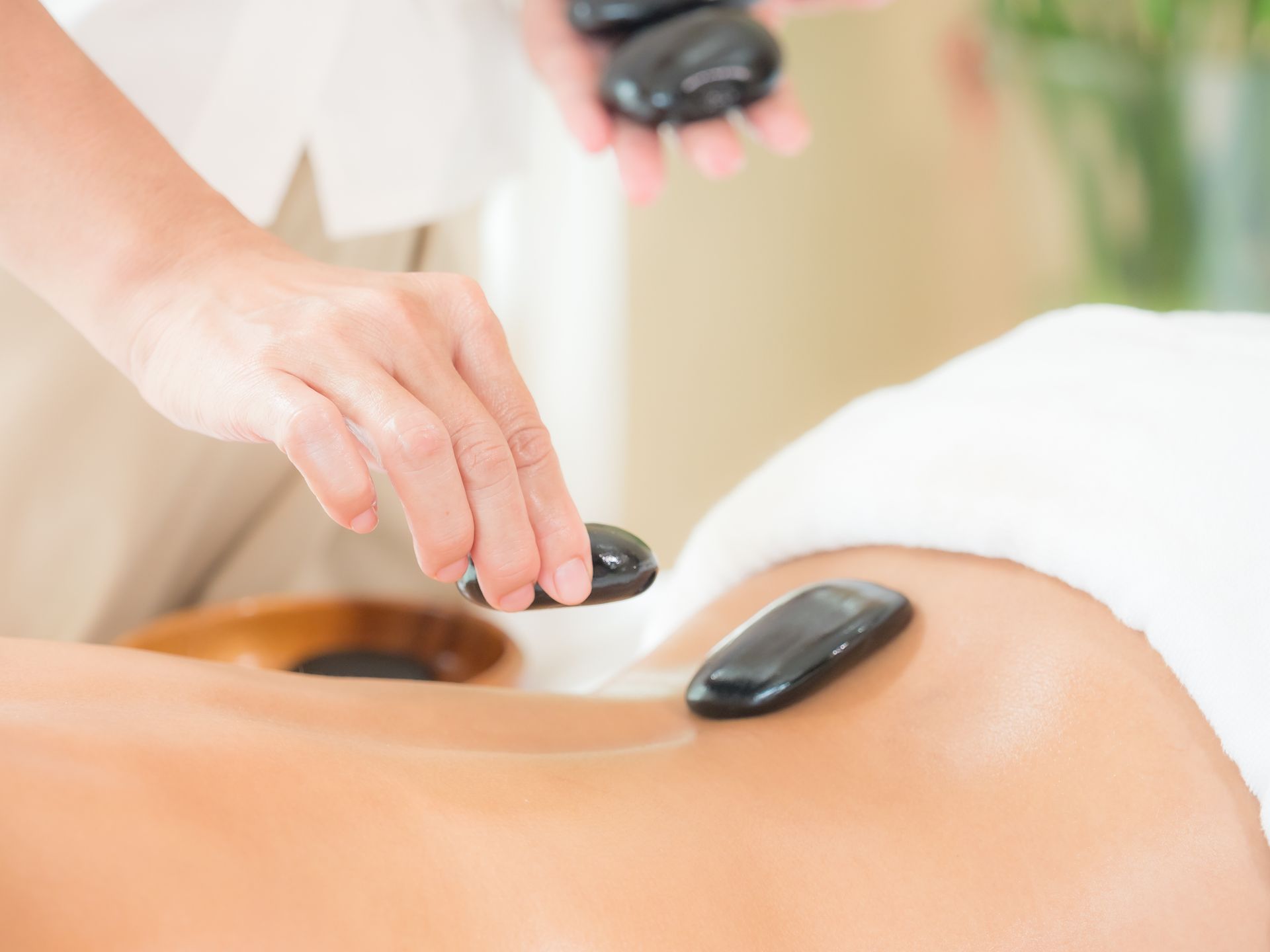 Hands placing heated black stones on a person's back during a spa treatment.