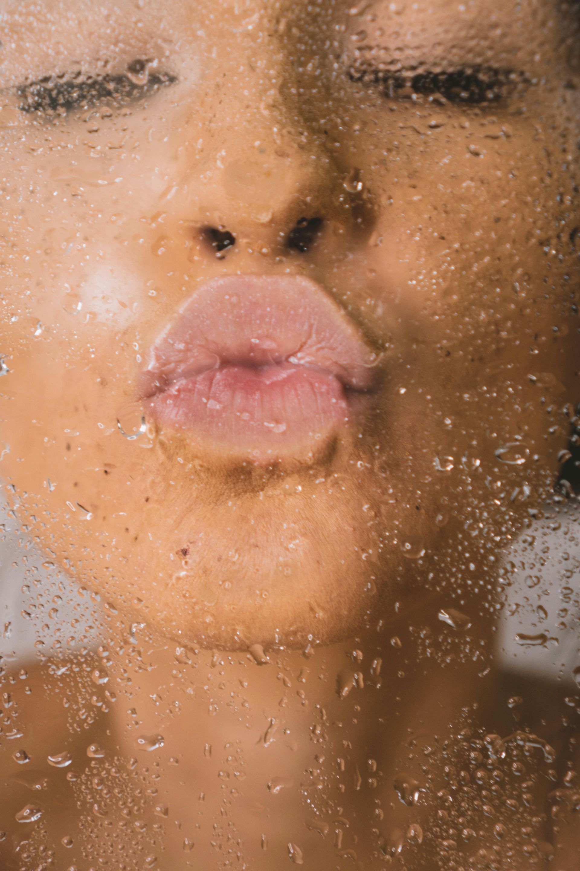 Face pressed against wet glass, lips pursed in a kiss. Water droplets cover the surface.
