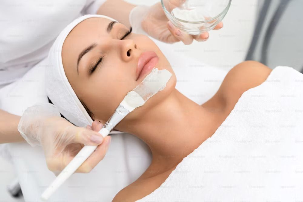 Woman receiving a facial treatment. A beautician applies a mask with a brush in a spa setting.