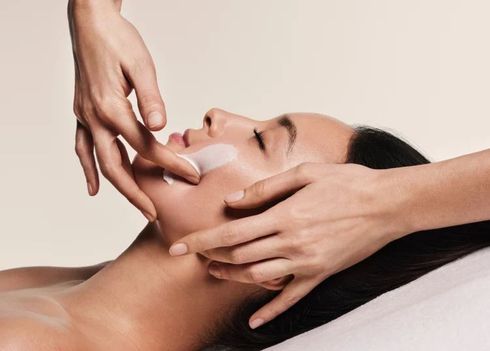 Hands applying cream to a person's cheek during a facial treatment.