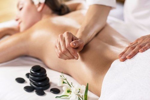 Woman receiving a back massage with hot stones. A person massages her back, spa setting.