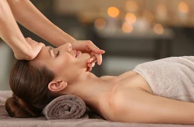 Woman receiving facial massage in a spa, hands on face, towel.