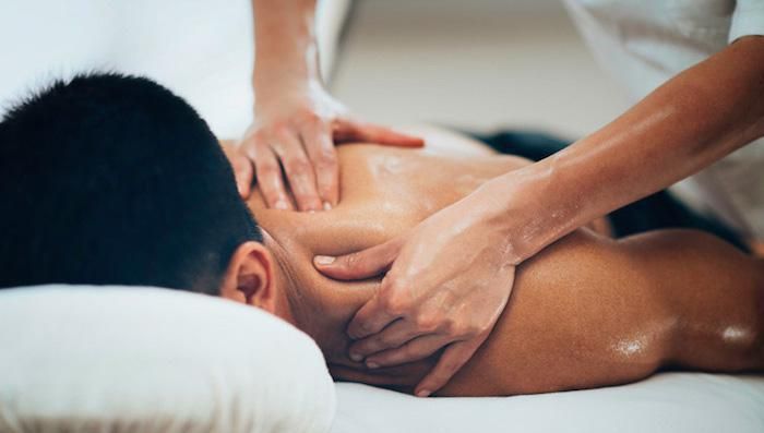 Woman receiving a back massage on a massage table, sunlight streams through a window.
