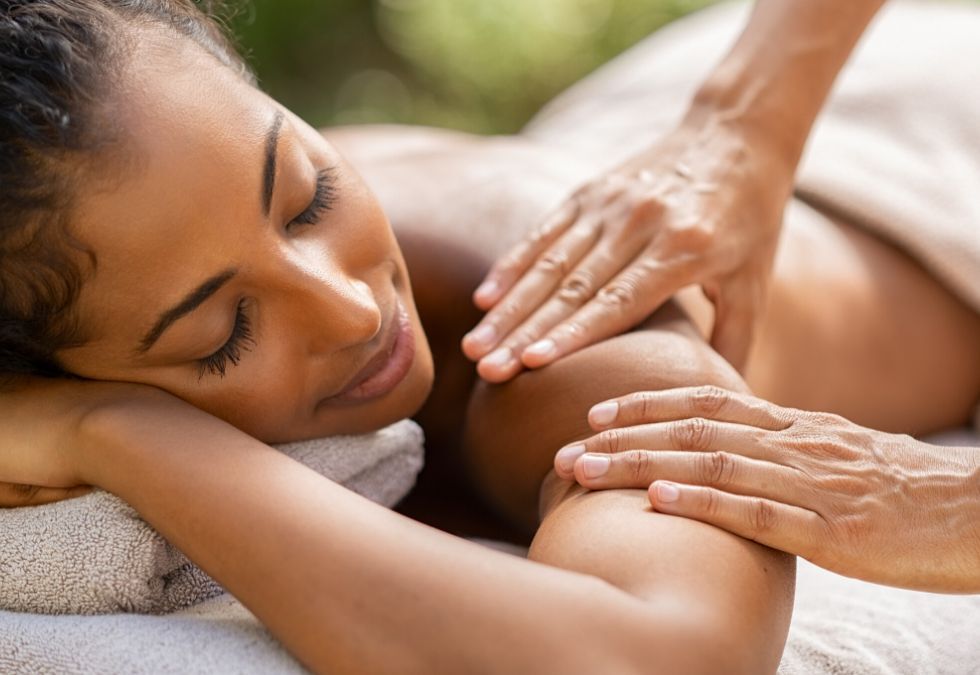 Woman receiving shoulder massage outdoors, eyes closed.