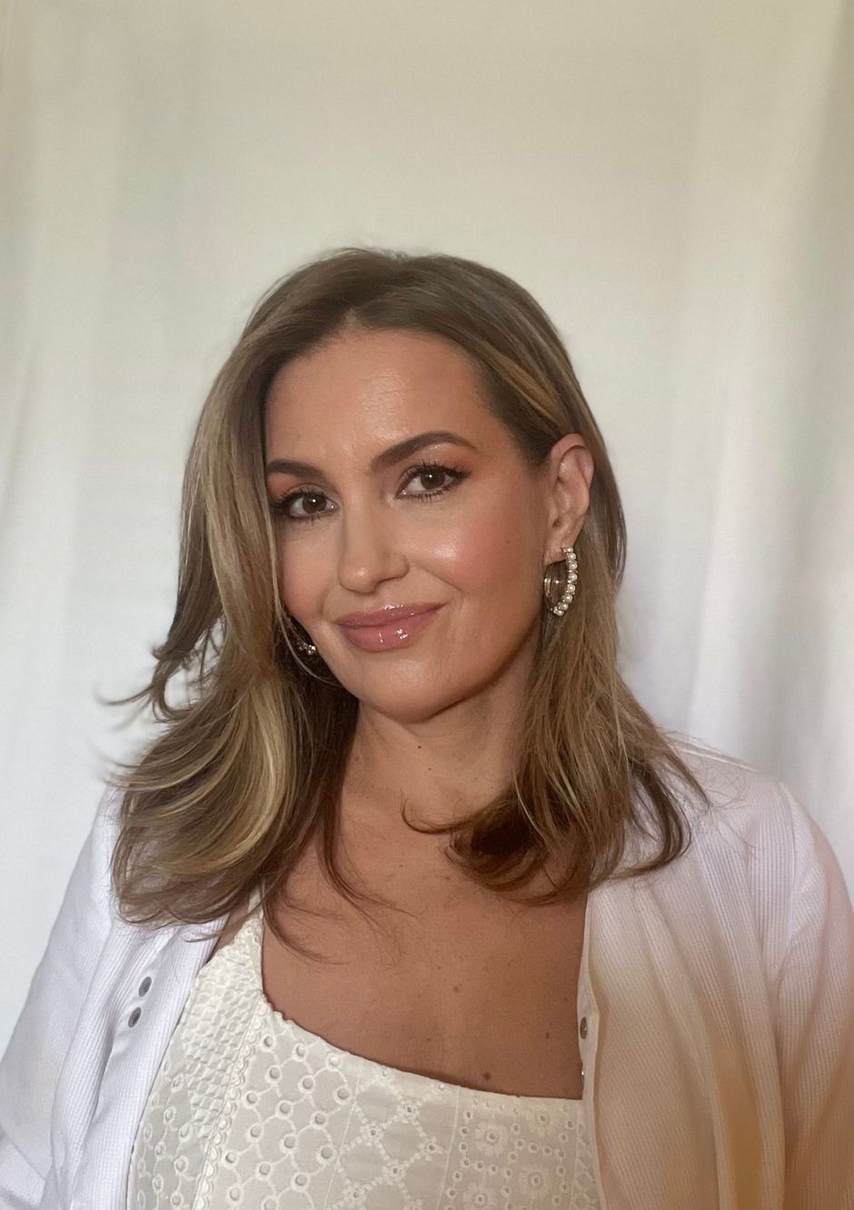 Woman with blonde hair, wearing a white top and cardigan, smiling, looking at the camera.
