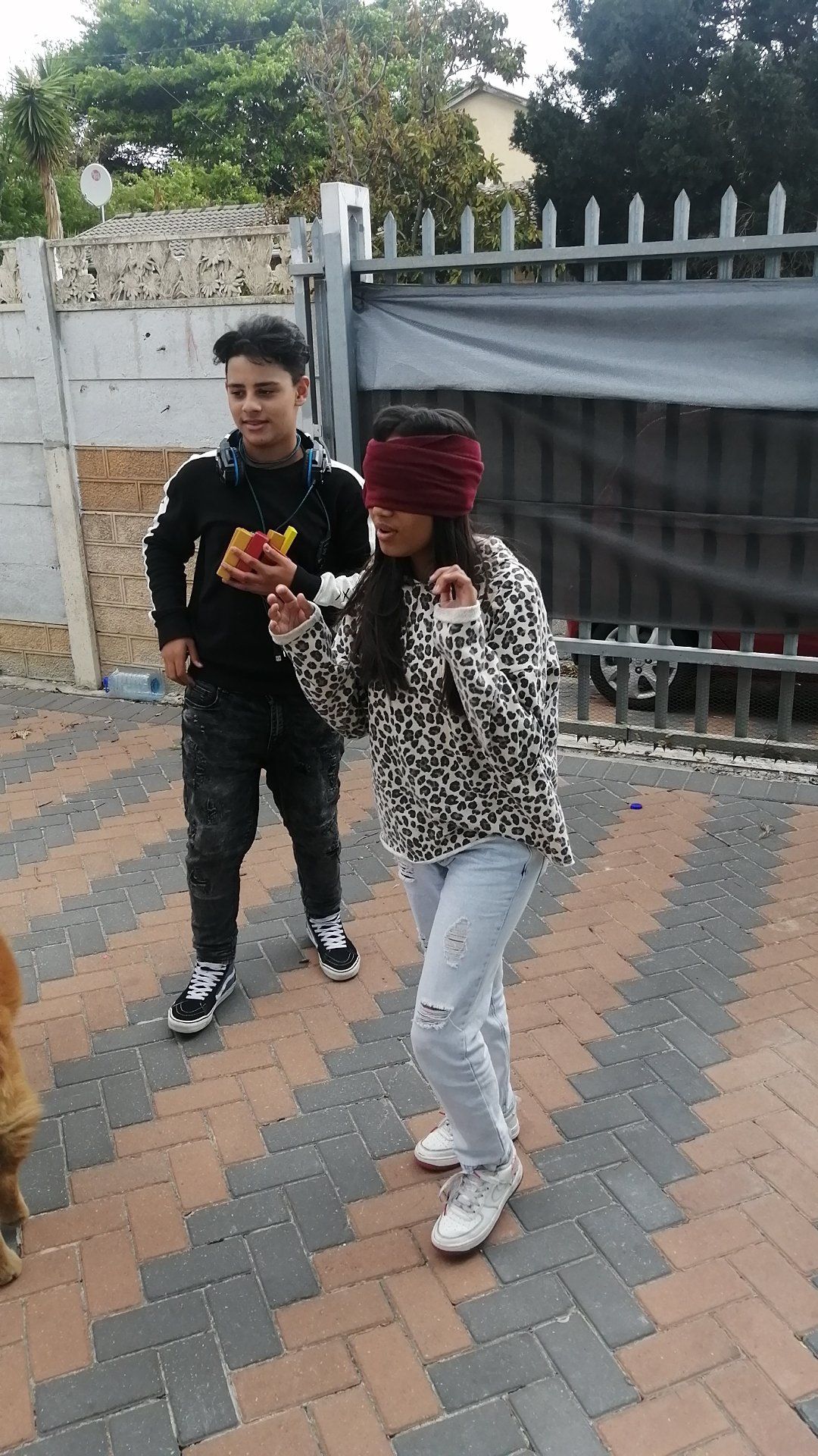 a boy and a girl are playing a blindfolded game on a brick sidewalk .