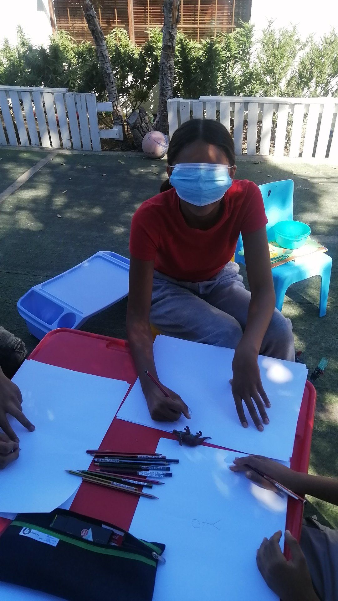 a girl wearing a mask is sitting at a table with other children .