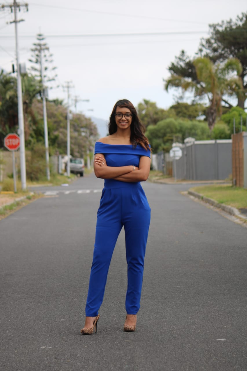 a woman in a blue jumpsuit is standing on a street with her arms crossed .