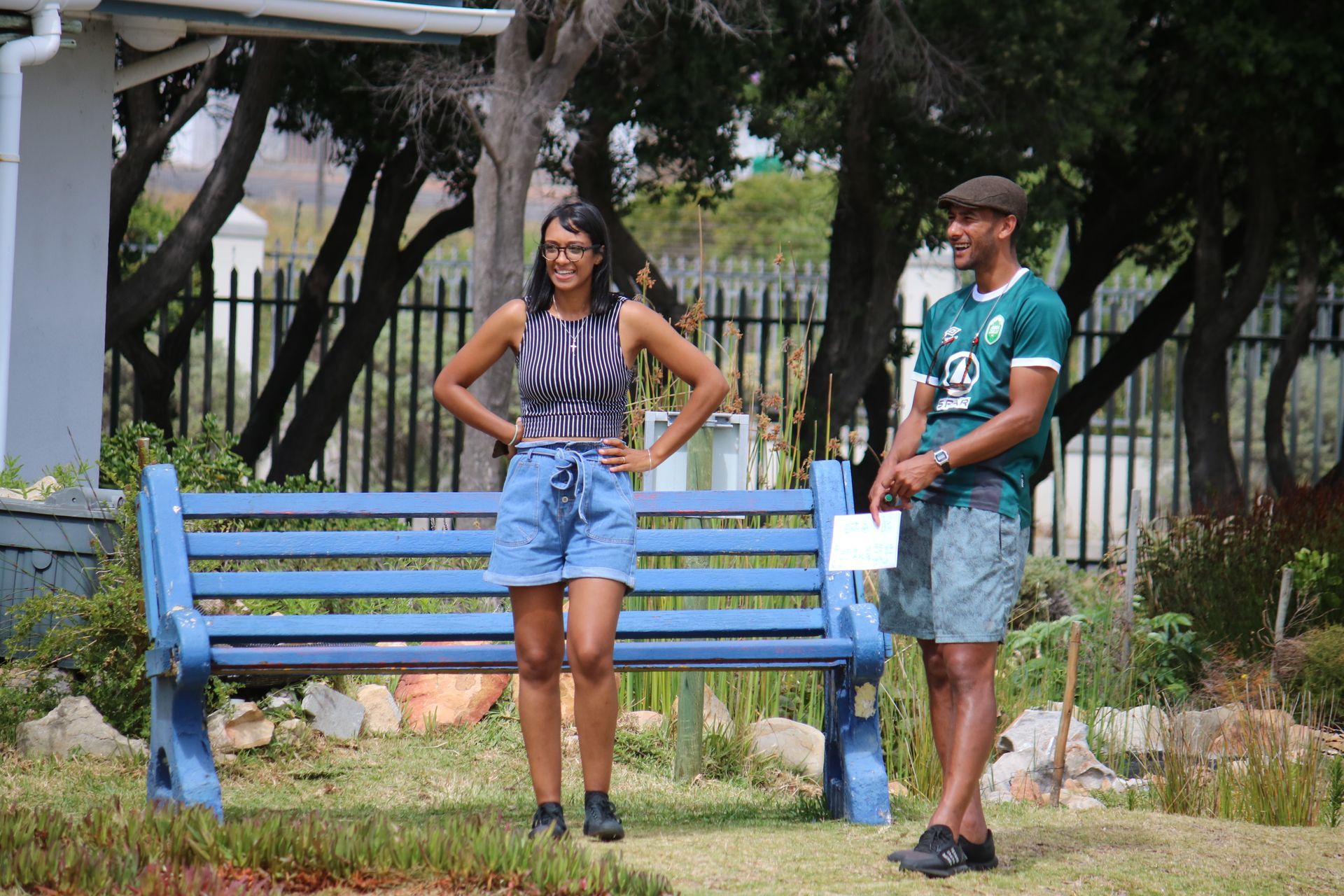 a man and a woman are standing next to a blue bench .