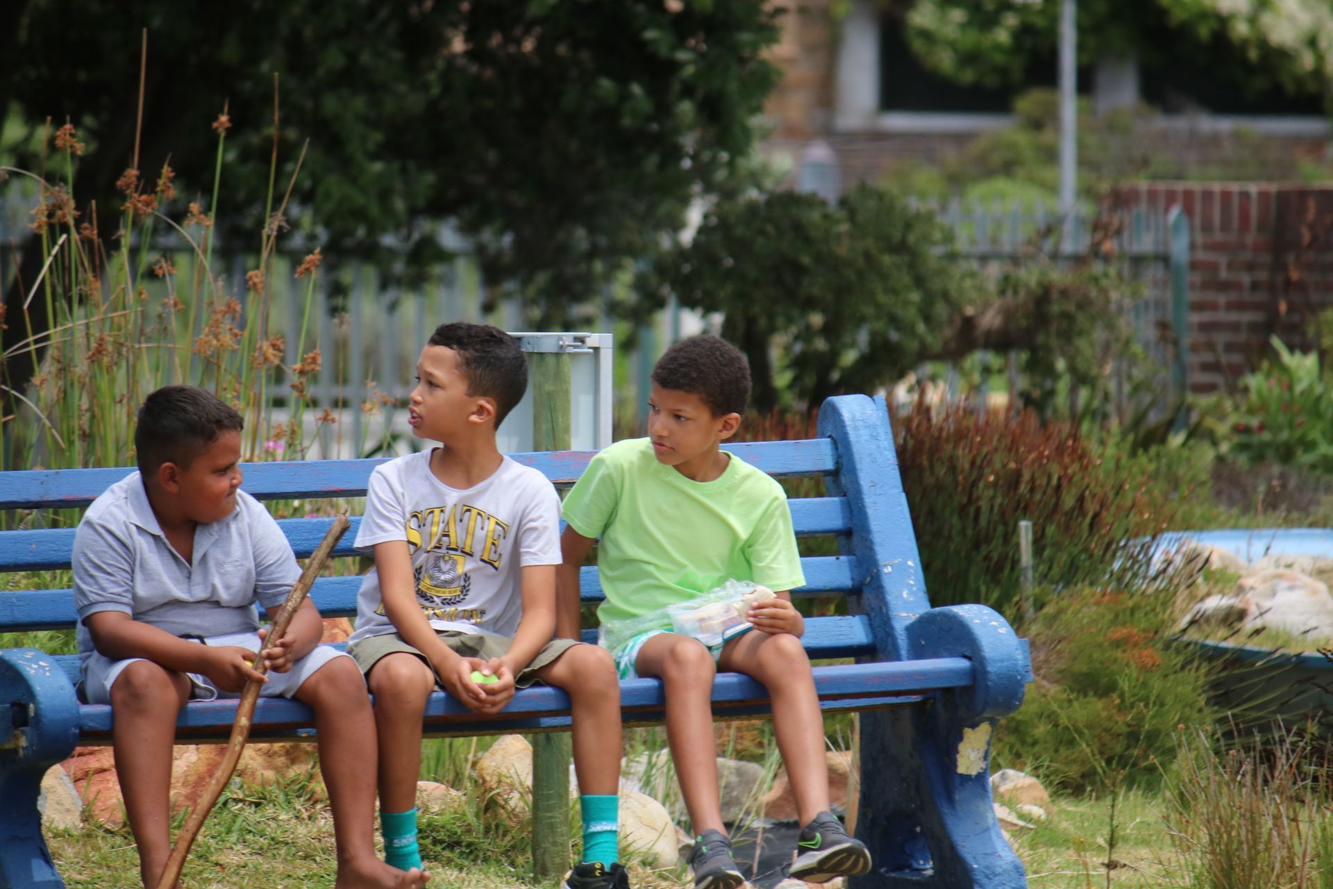 three young boys are sitting on a blue bench talking to each other .