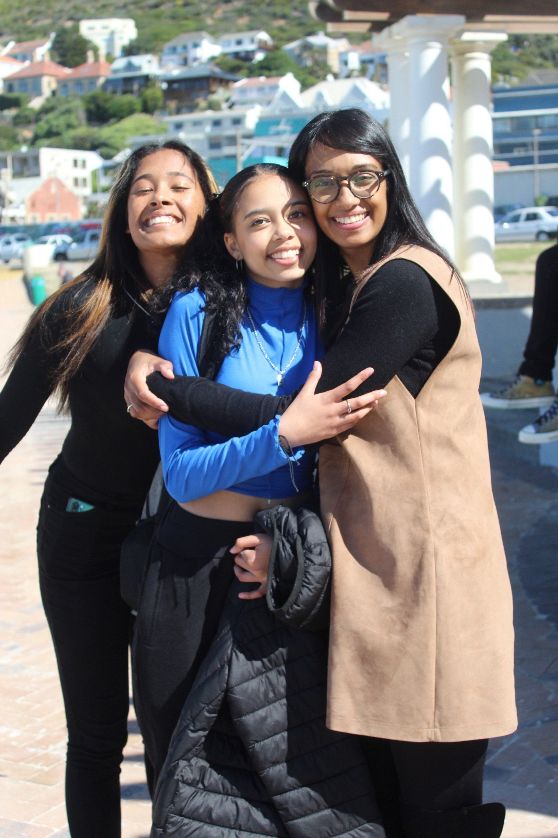 three young women are posing for a picture and hugging each other .