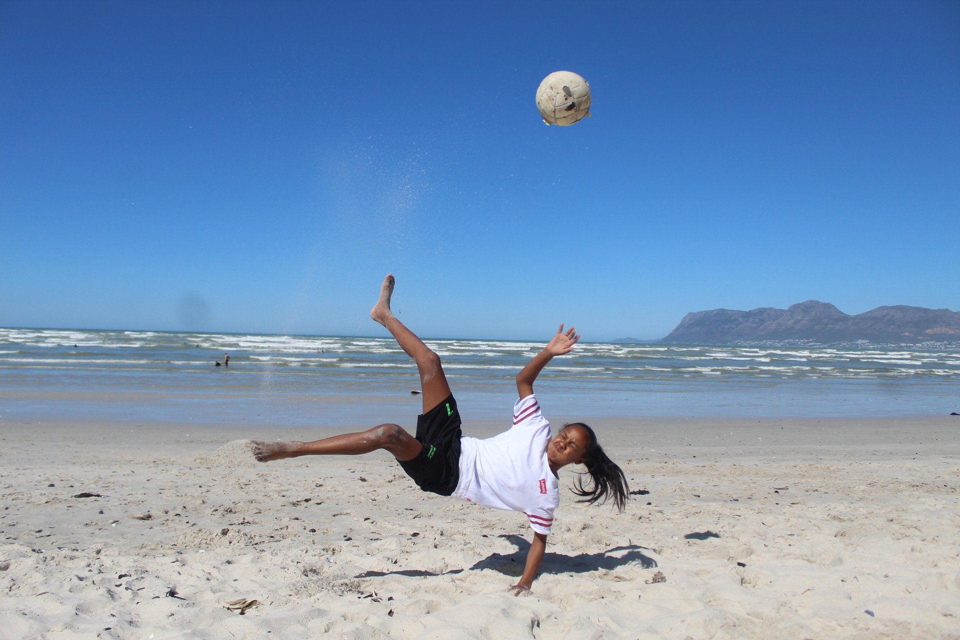 a person is doing a handstand on the beach while kicking a soccer ball