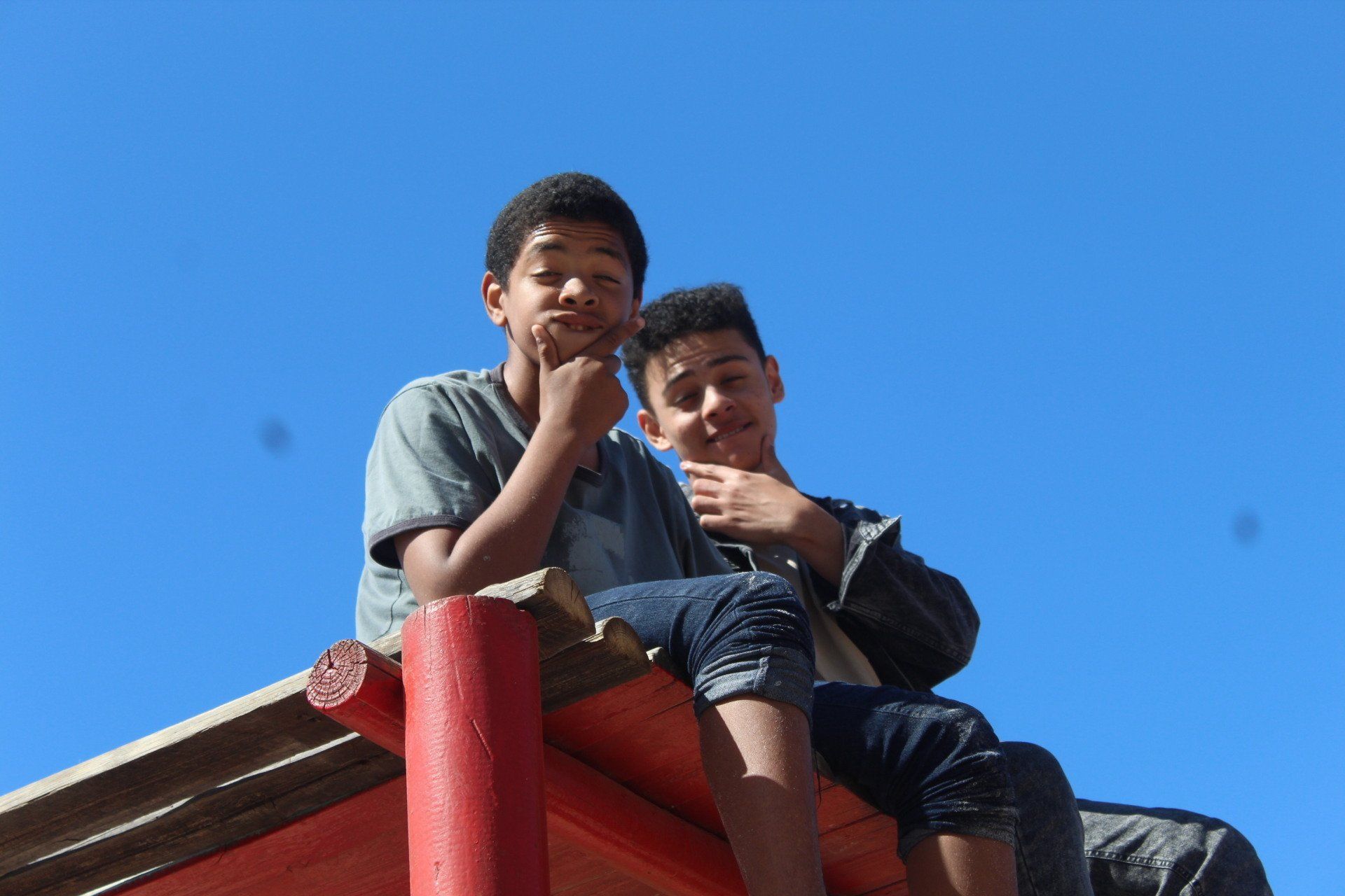 two young boys are sitting on top of a wooden structure .