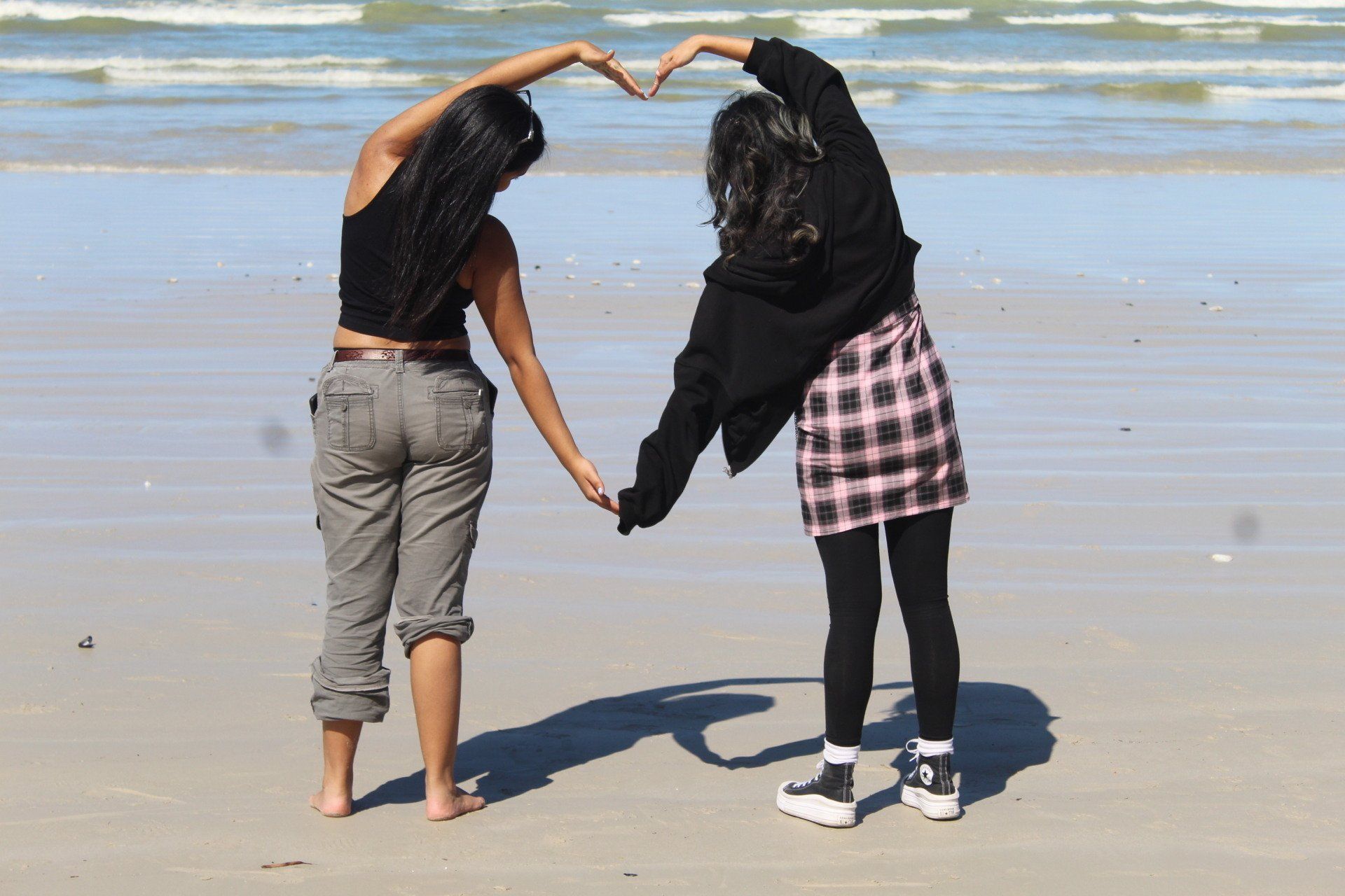 two women are making a heart shape with their hands on the beach .