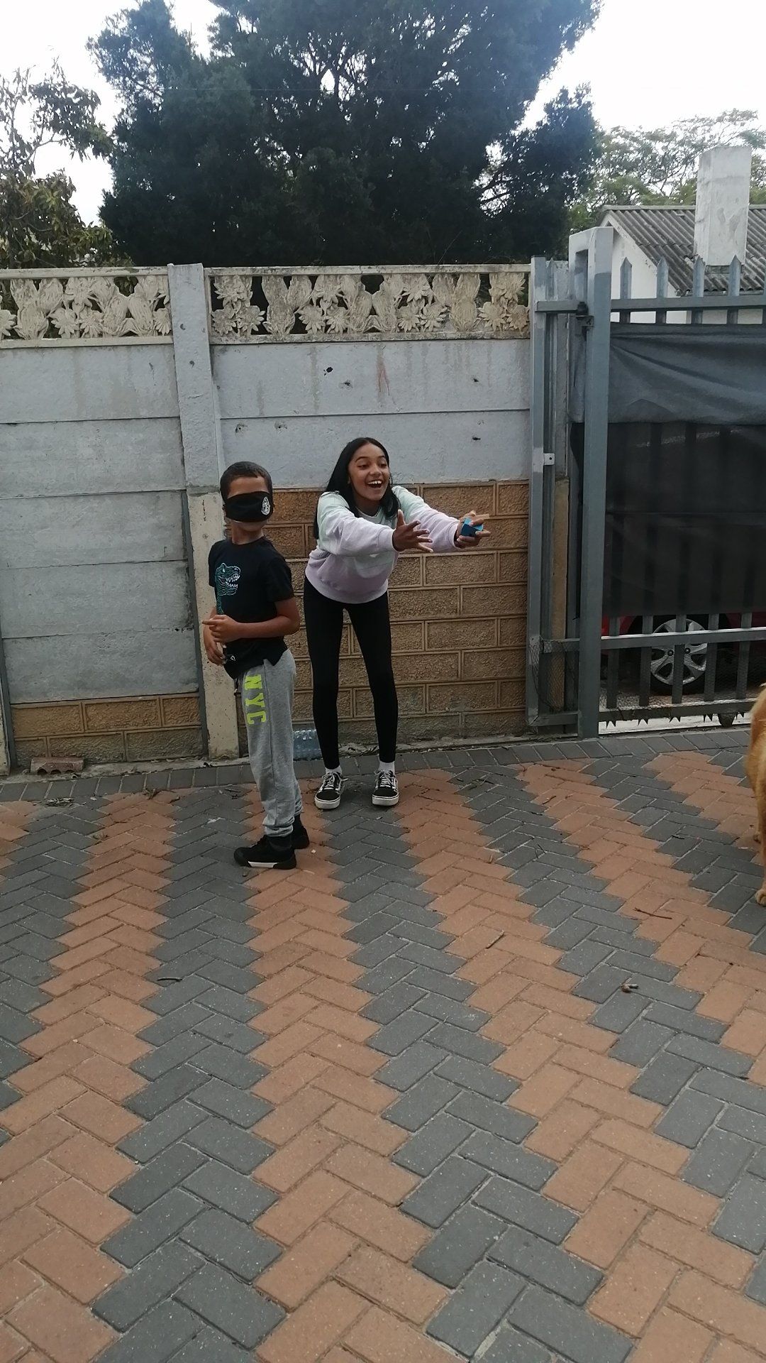 a boy and a girl are standing on a brick driveway .
