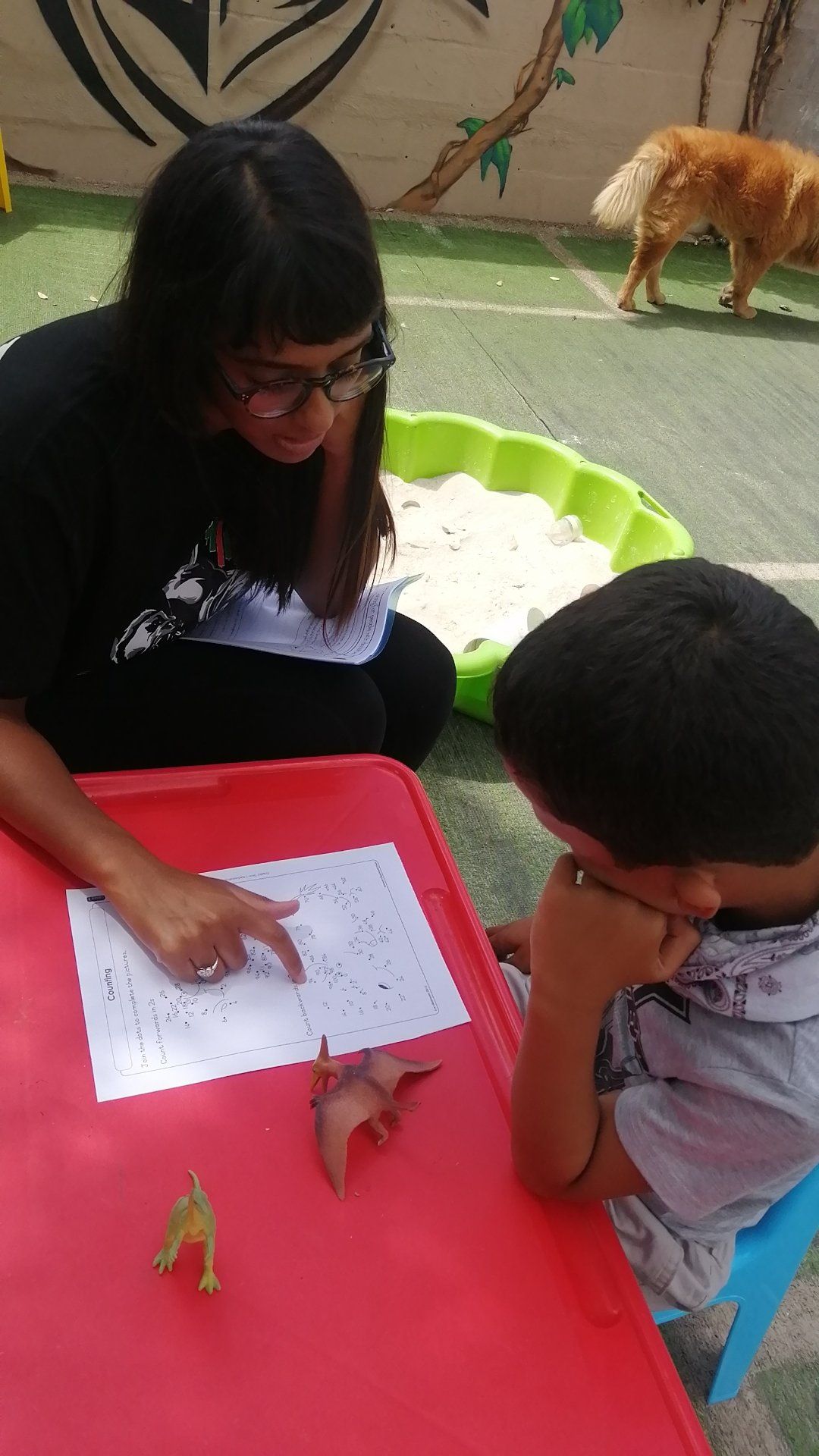 a woman is sitting at a table with a child and pointing at a piece of paper .