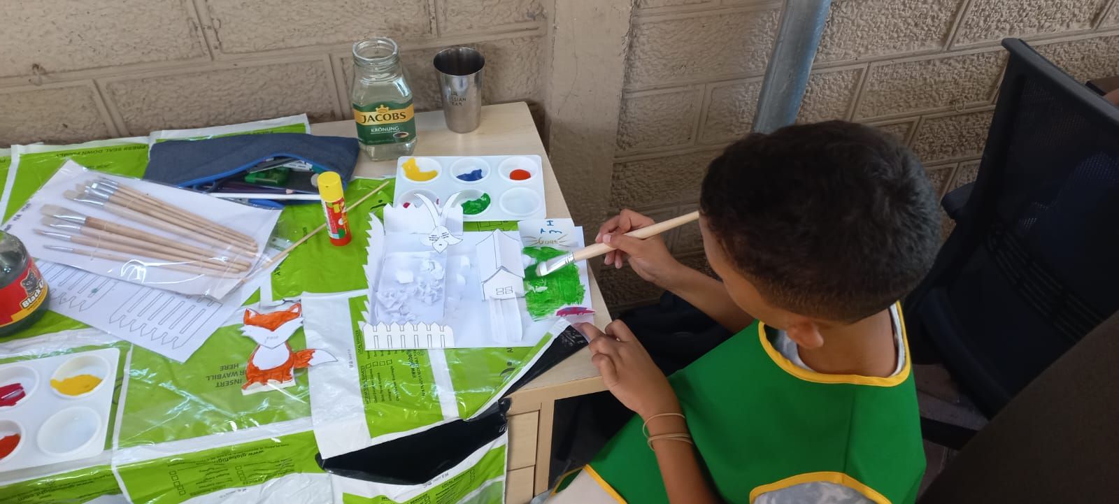 a young boy is sitting at a table painting with a brush .
