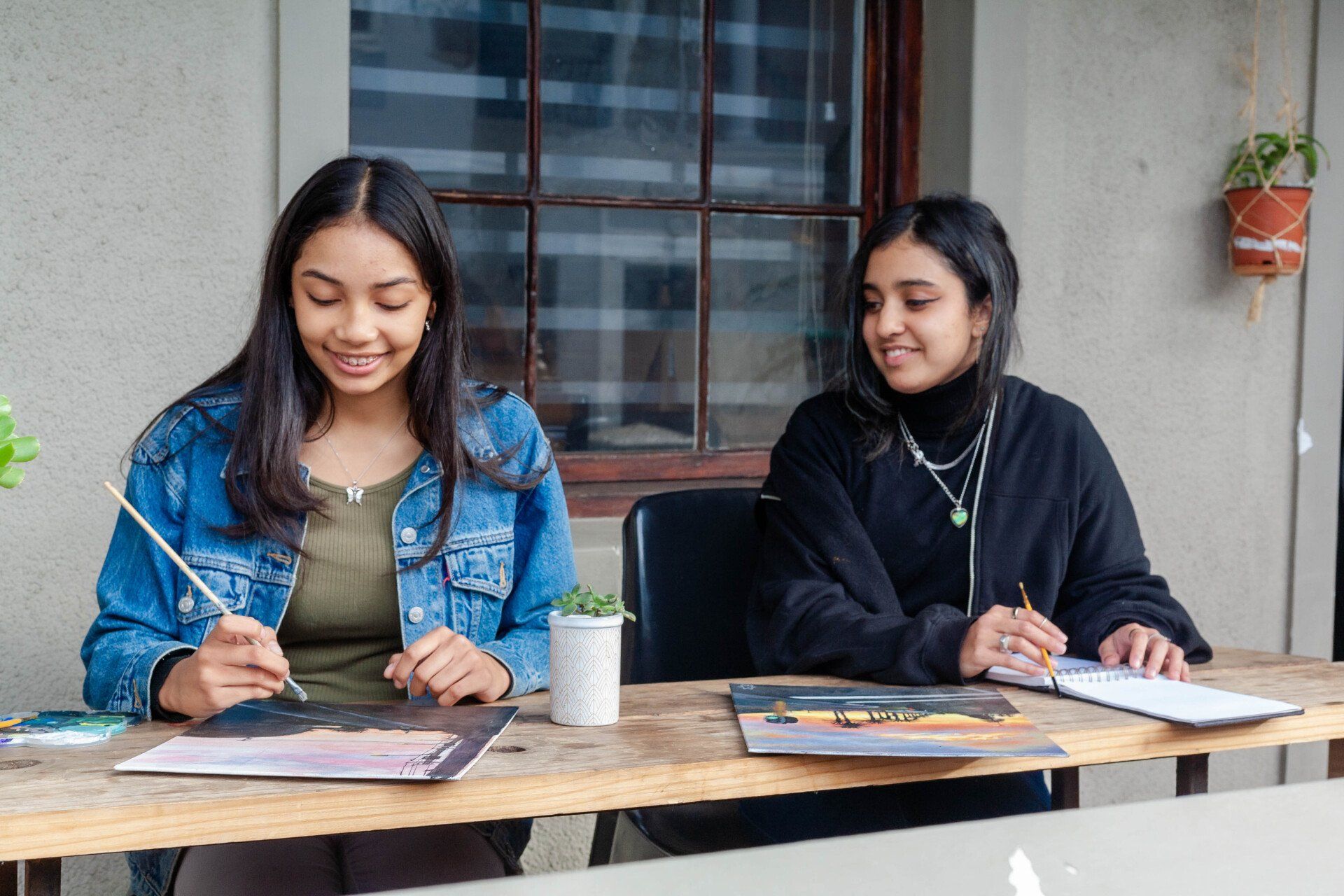 two women are sitting at a table painting .