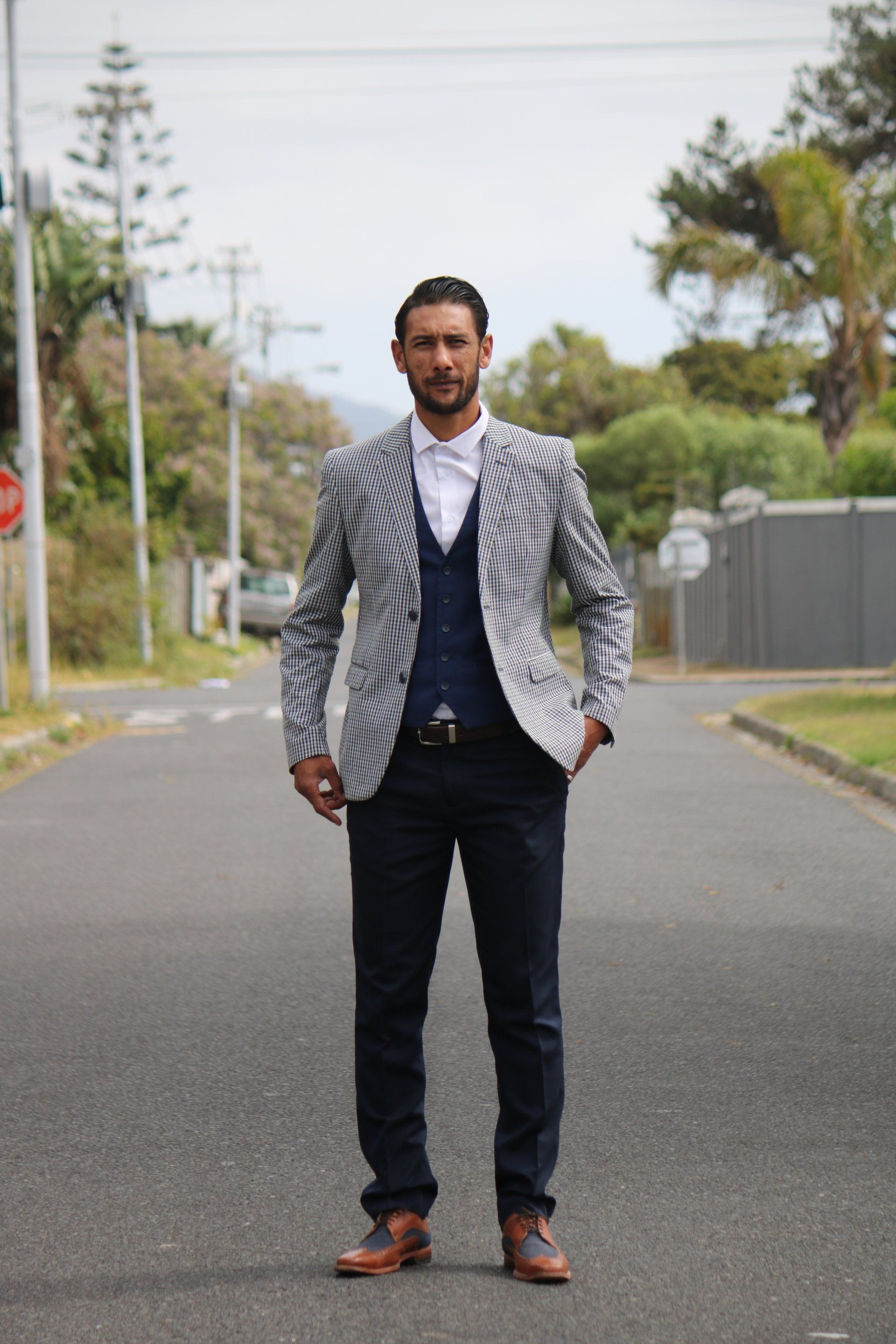 a man in a suit is standing on a street with his hands in his pockets .