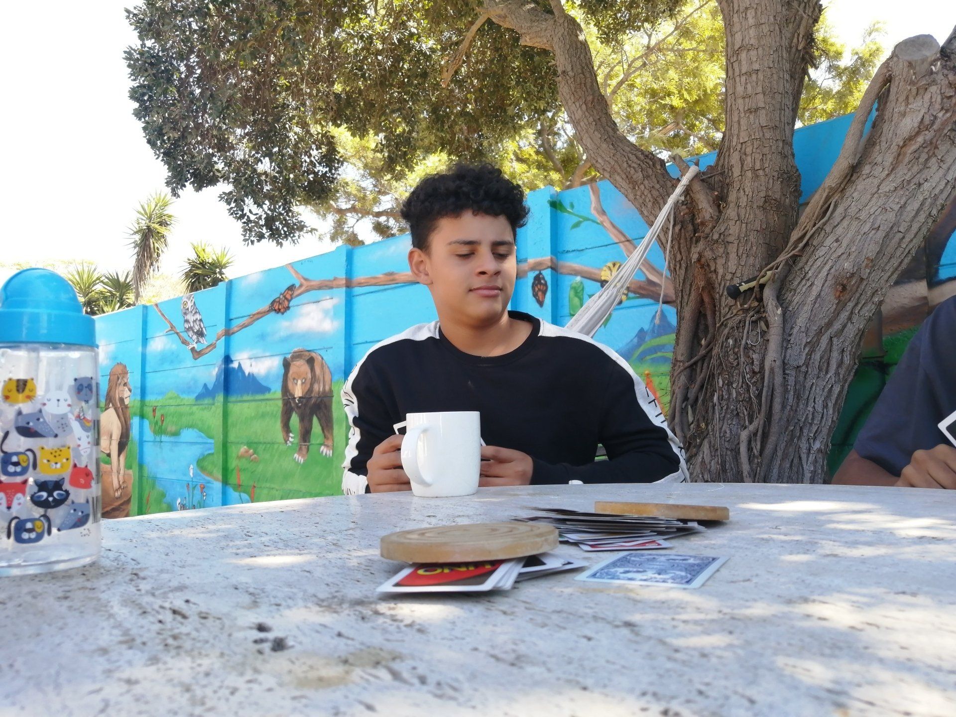 a boy is sitting at a table holding a cup of coffee .