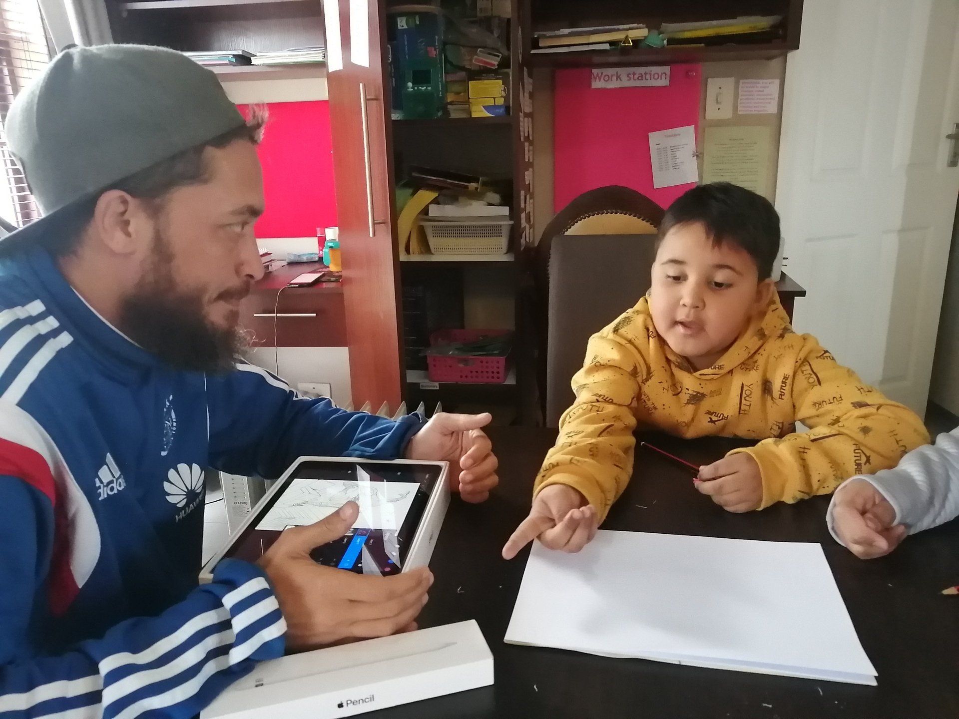 a man and two children are sitting at a table looking at a tablet .