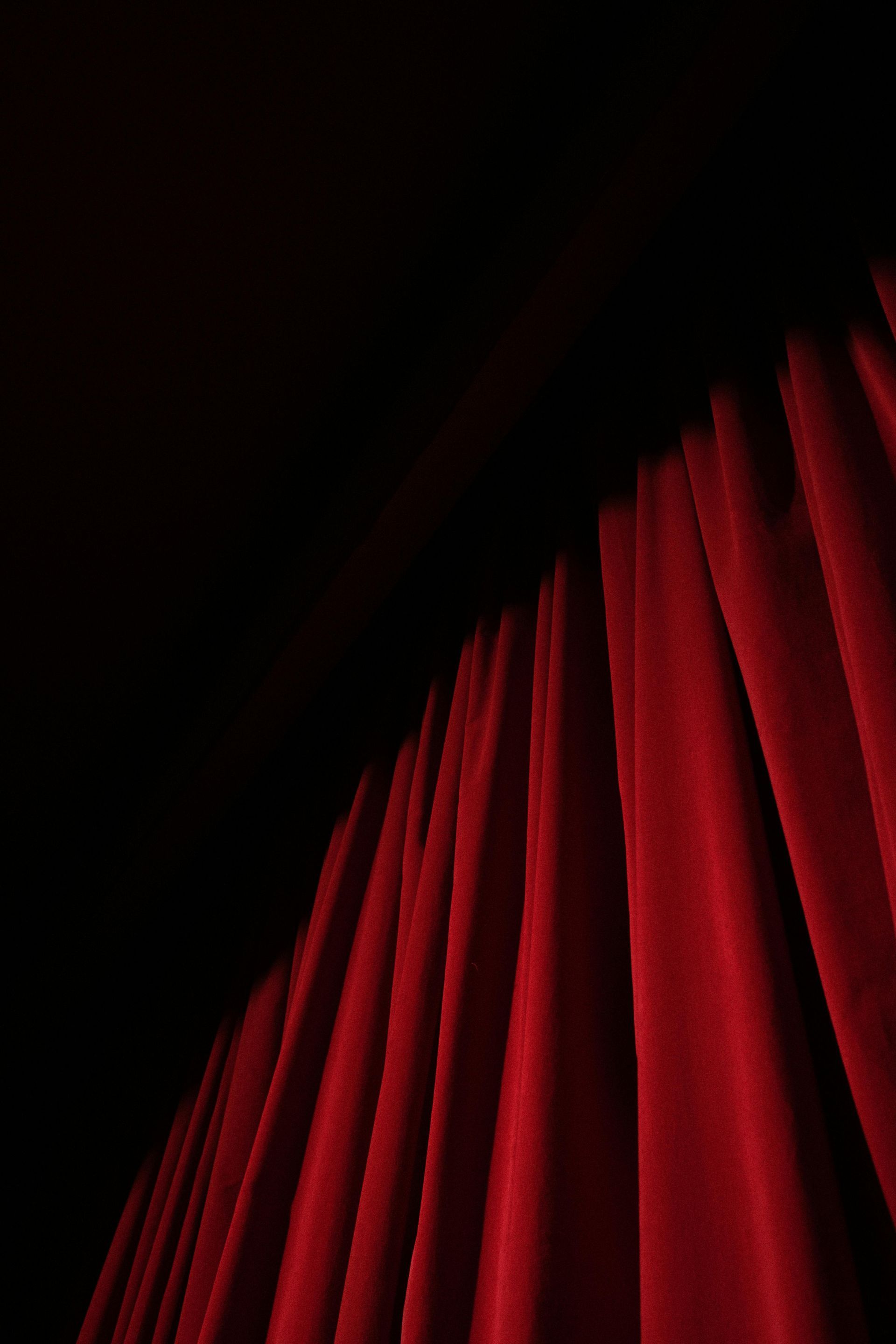 Red velvet stage curtain partially drawn, revealing a dark space.