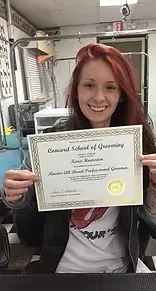 Woman with red hair, smiling, holding a dog grooming certificate.
