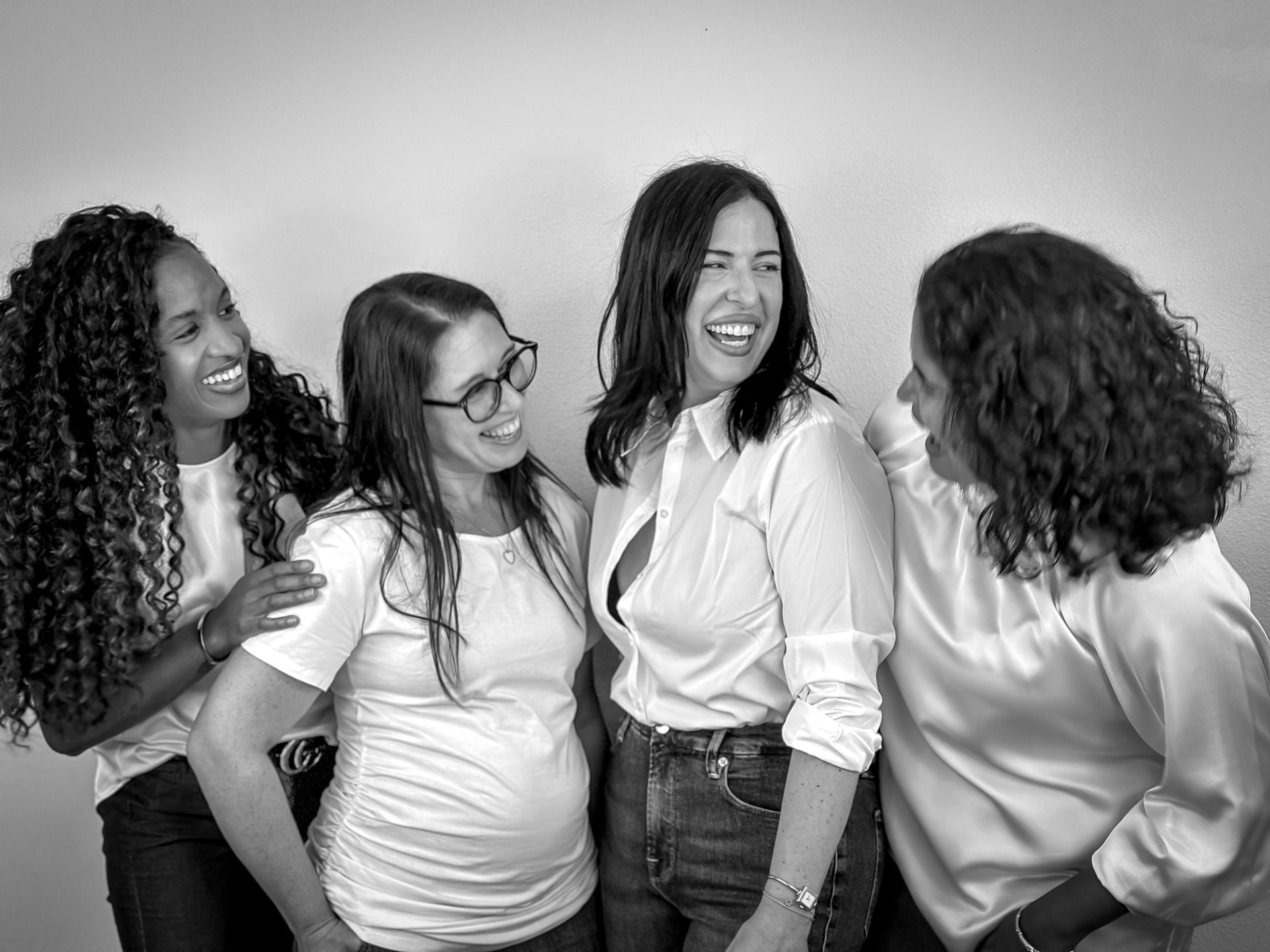 A group of women are standing next to each other and laughing in a black and white photo.
