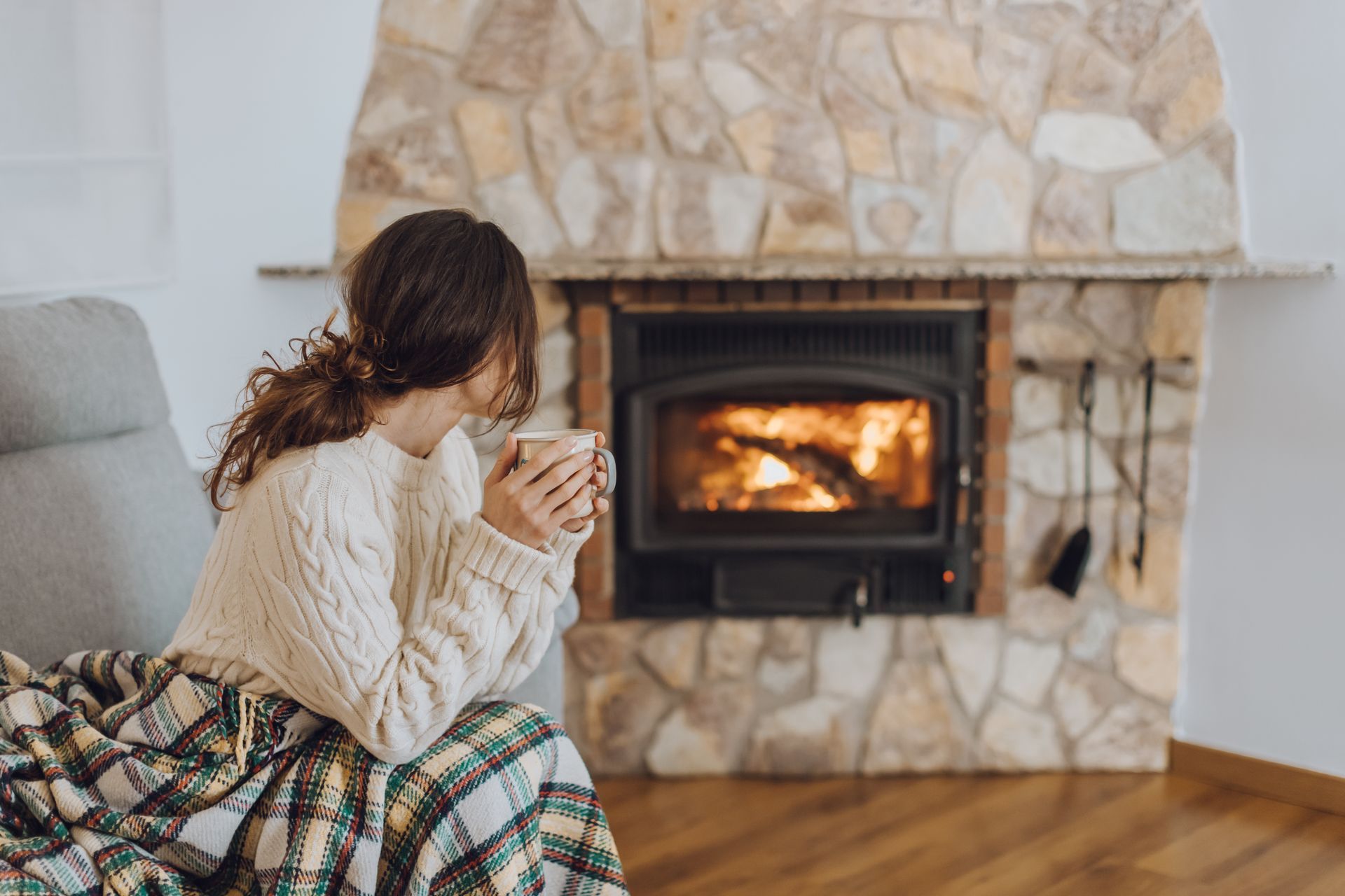 A woman is sitting in front of a fireplace holding a cup of coffee.