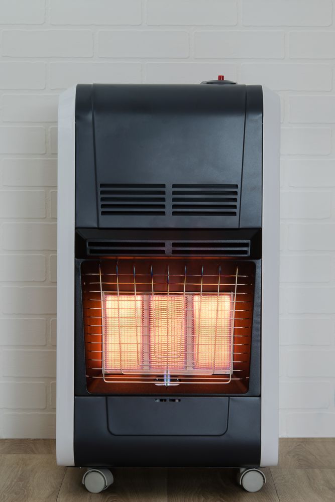 A gas heater is sitting on a wooden floor in a room.
