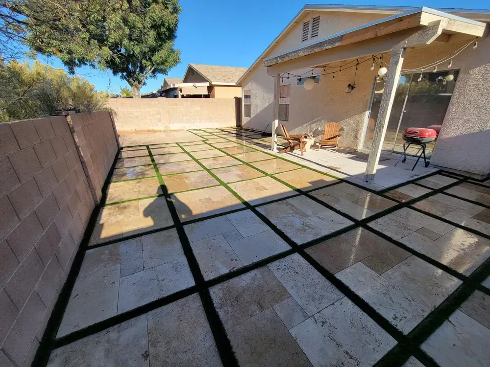 Backyard patio with travertine tiles and artificial turf grid, outdoor seating, and a grill.