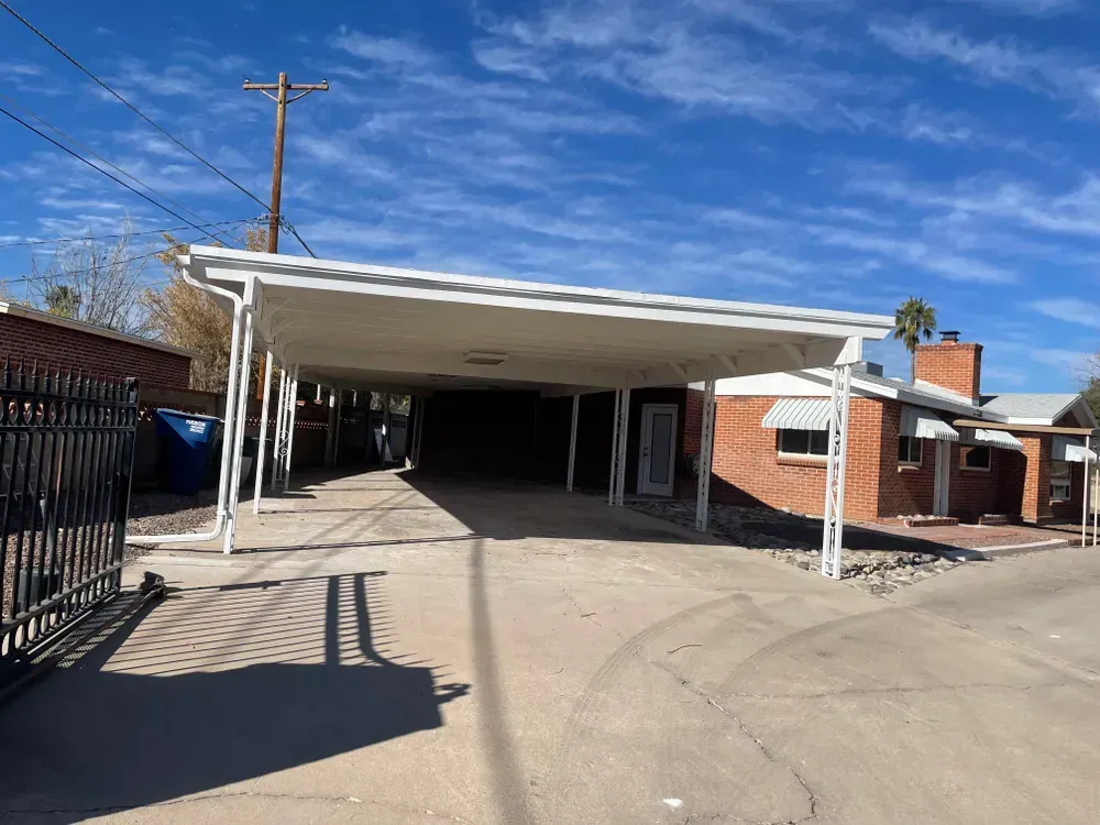 White carport over a driveway, next to a red brick building, against a blue sky.