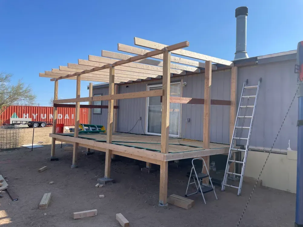 Wooden deck construction in progress next to a light-colored building with a pergola.