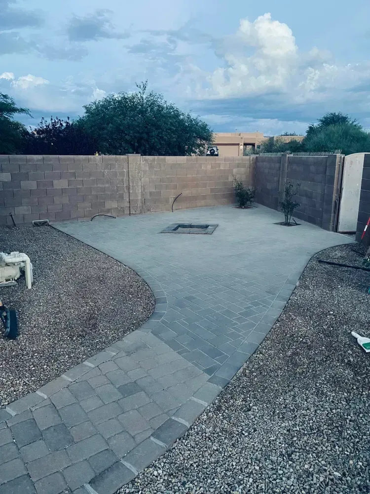 Backyard patio with paved pathway, fire pit, and gravel landscaping, enclosed by a brick wall.