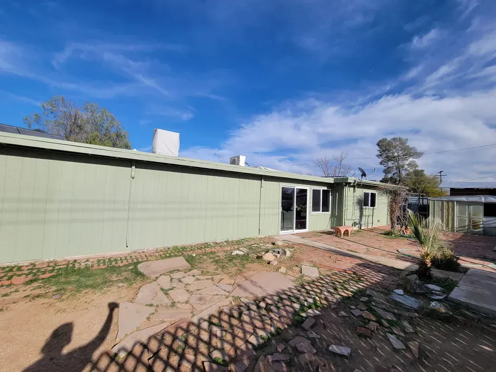 Green house exterior with sliding glass doors, blue sky, and patchy yard.