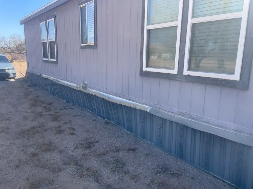 Exterior of a light purple mobile home with blue siding on a dirt lot. White window frames.