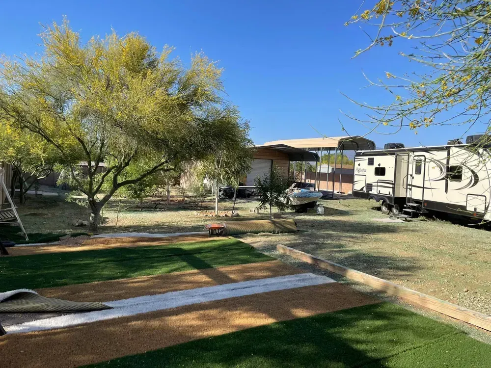 Backyard with RV, tree, car, and artificial turf in a sunny setting.