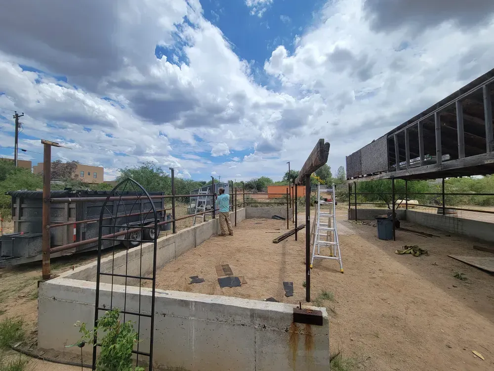 A person standing in a dirt yard with concrete borders and structures under a cloudy sky.