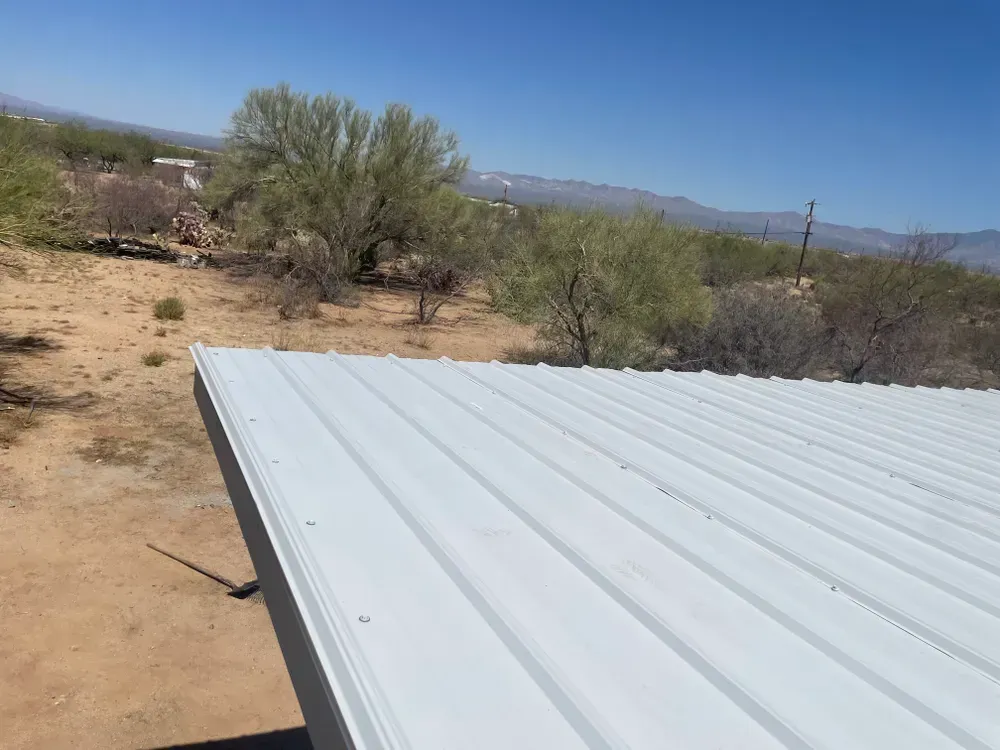 White metal roof edge with arid landscape, blue sky, and distant mountains.