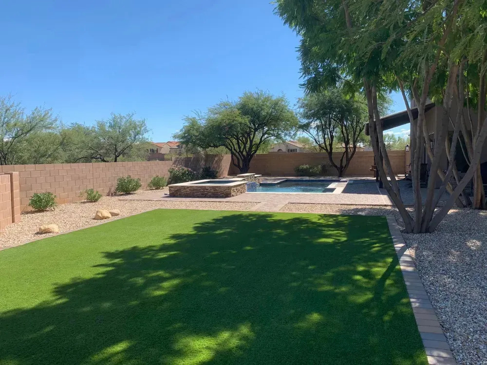 Backyard with pool, hot tub, and artificial grass under a sunny blue sky.