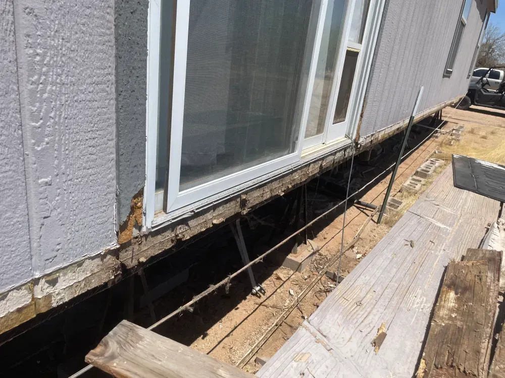 Exterior view of a house undergoing repair work; exposed foundation, siding, and sliding glass door.