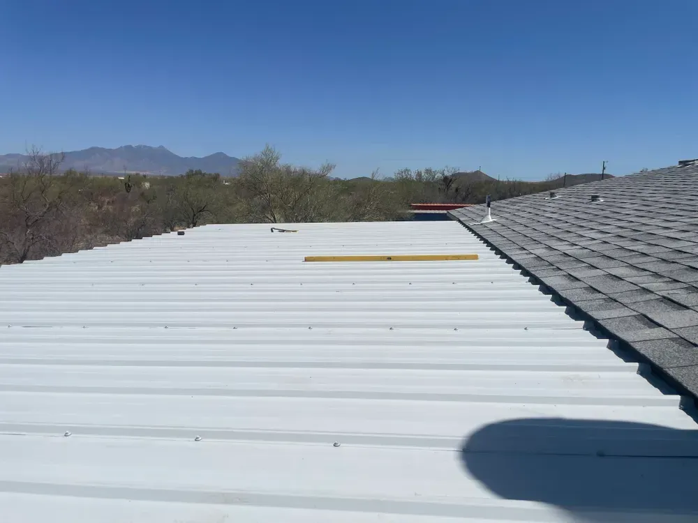 White metal roof next to a grey shingle roof with a mountain backdrop.