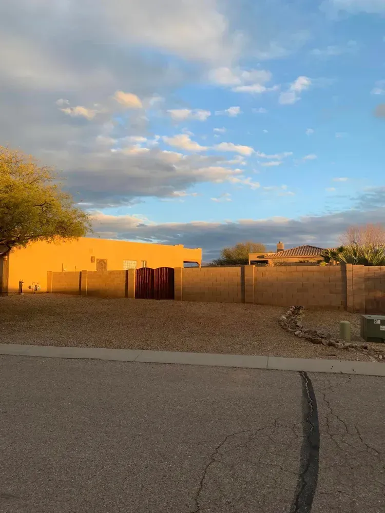Desert landscape with a long wall and buildings bathed in warm sunlight under a blue and cloudy sky.