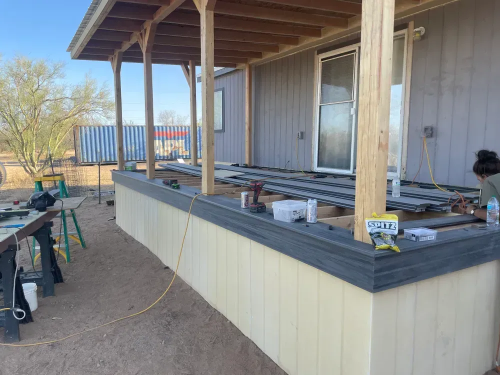 Porch construction: composite decking, wooden posts, tan siding, person working on the deck.