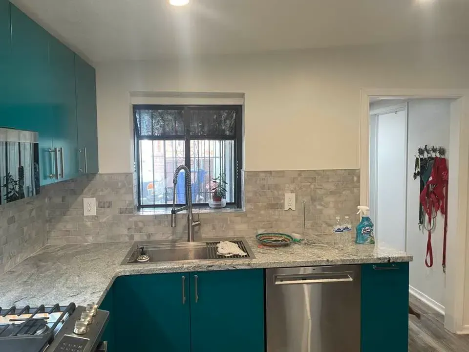 Kitchen with teal cabinets, a stainless steel sink, and a window with a view. Granite countertop.
