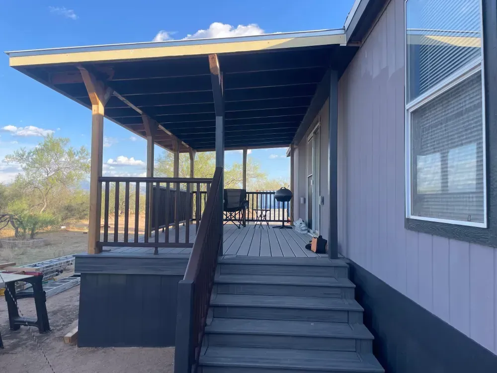 Covered porch with stairs leading up to a house. Gray siding, blue sky.