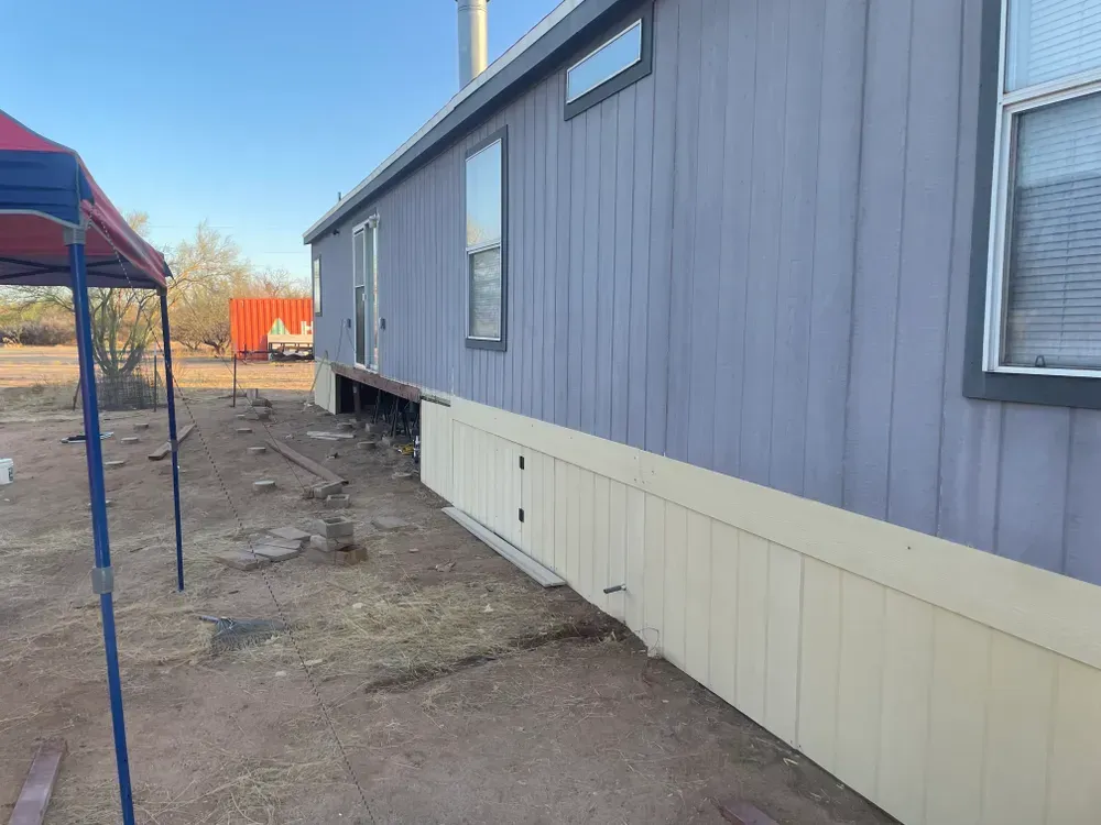 Mobile home with gray siding and tan skirting in an outdoor setting.